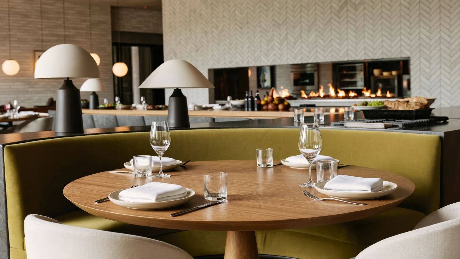 Restaurante contemporáneo con mesa de madera, asientos verde oliva y cocina abierta con fuego; imagen aportada por el estudio.